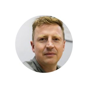 A circular headshot of Neil Crook Media Producer and Editor, Megger looking down the lens of the camera