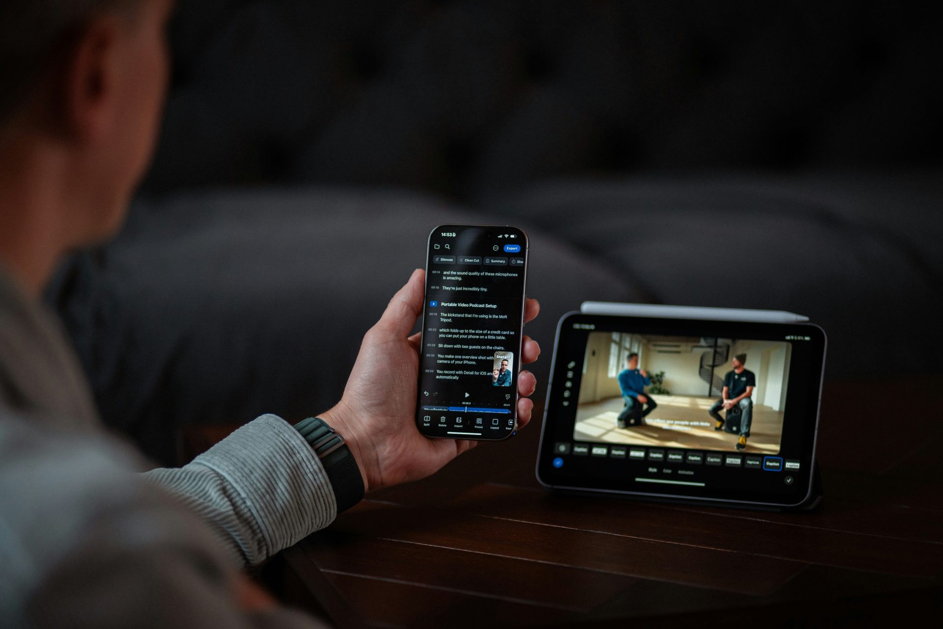 detail-co-JDmZK2I8DRk-unsplash Over the shoulder shot of someone holding their phone with a transcript on while a tablet shows a video to the right