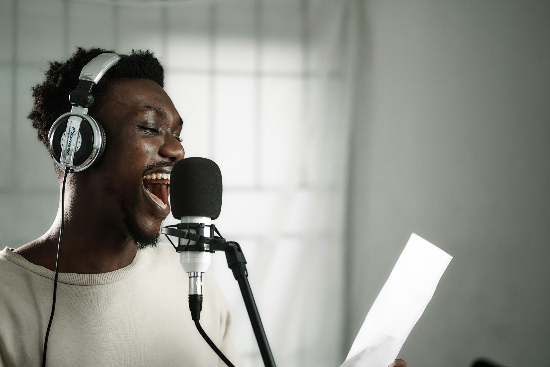 emmanuel-ikwuegbu-n_qhPU-nsyc-unsplash A voice over artist with headphones on is looking at his lines and smiling in front of a black microphone