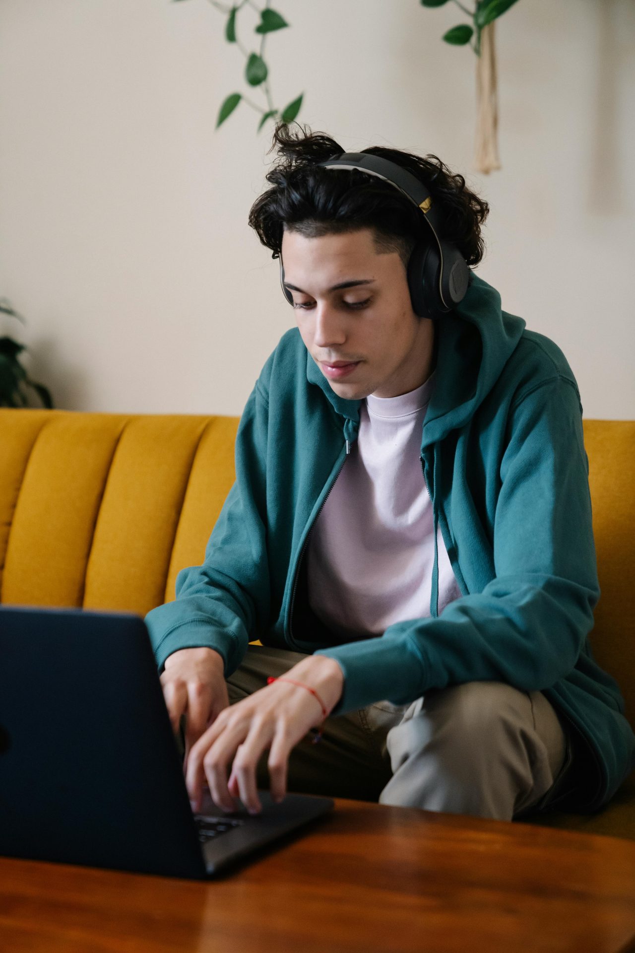 pexels-eren-li-7241683 Portrait shot of a man with headphones on sat on a yellow sofa and on his laptop