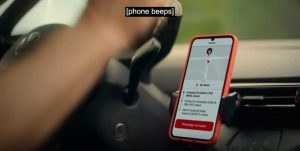 Phone in a holder to the right of steering wheel showing maps that say 'Arrived'. SDH at the top of the screen reads [phone beeps].