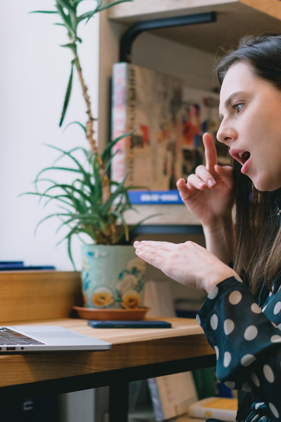 VB Website 11 Portrait image of a woman with dark hair and a spotted top performing sign language with her hands in the direction of a laptop