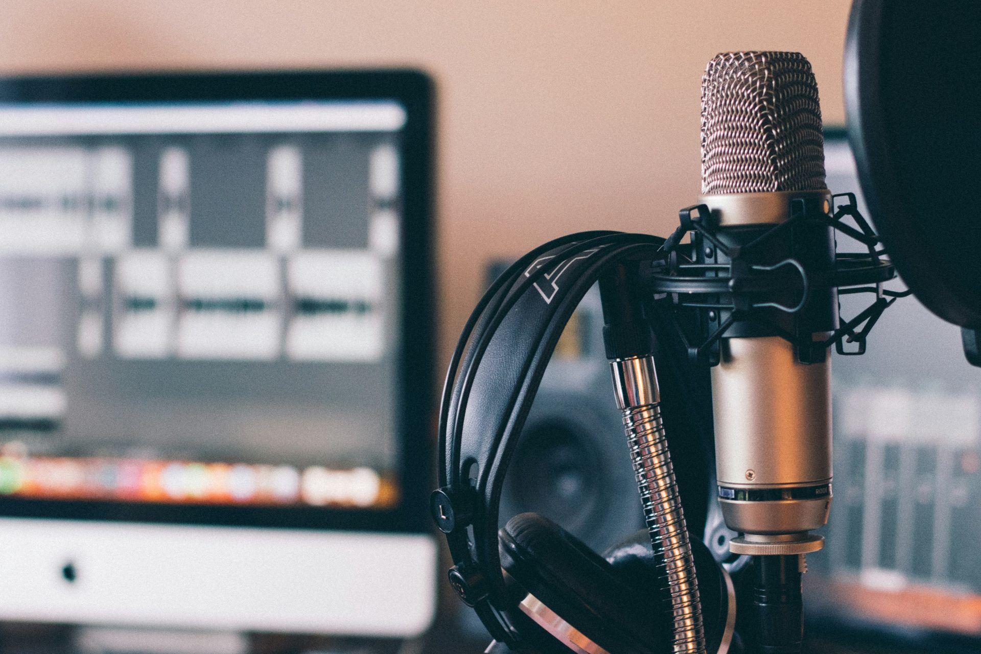 will-francis-ZDNyhmgkZlQ-unsplash Black headphones are hanging on a silver microphone to the right of the close up. In the background is an IMac